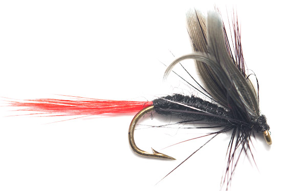 Fluga för flugfiske skapat av fina flugbindningsmaterial i rött och svart placerad på en vit bakgrund.
